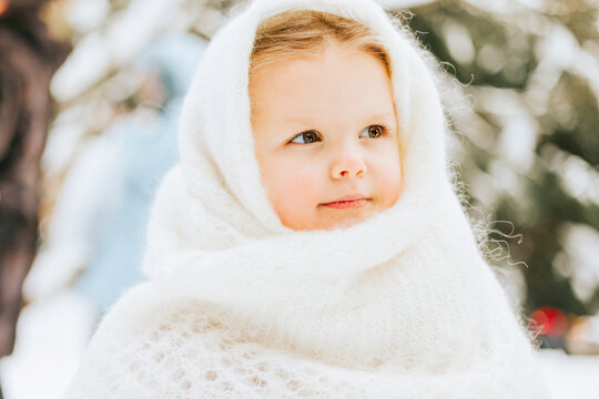 portrait cute little girl toddler in white russian style orenburg down shawl scarf in snow winter forest, concept of Christmas holidays and New Year in retro vintage style