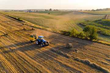 Golden and green fields with blue tractor making hay bales. Farming and agriculture. Natural landscape. Horizontal shot. High quality photo