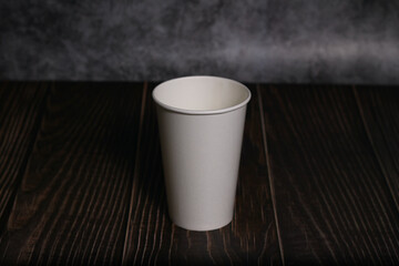 white empty take away coffee cup with blank copy space for design text or banner of brand, hot drink on wooden table and blurred grey wall background