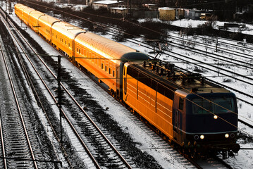 Lok und Waggons eines Personenzugs fahren orange von der untergehenden oder aufgehenden Sonne angestrahlt diagonal durch das Bild