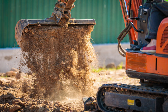 A minitractor rakes the earth with a bucket. Land works.