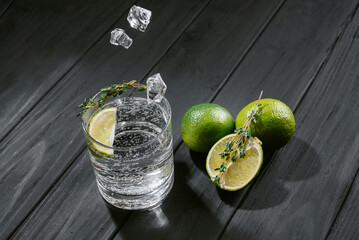 hard seltzer with lime on a dark wooden background, ice cubes fall into a glass with an alcoholic...