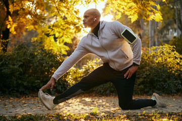 Young black sportsman stretching his leg during sports training in autumn park.