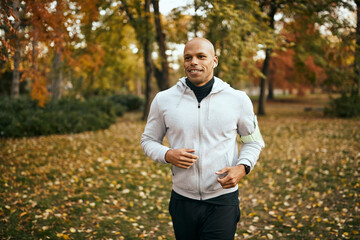 Happy black sportsman running in park on autumn day.