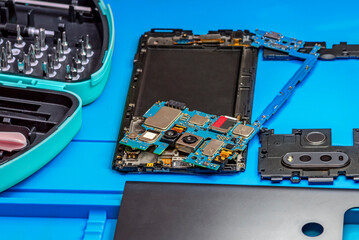 Smartphone repair in a service center. Hands of a professional master repairman repairing disassembled into pieces cell phone. Internal parts, chips, motherboards, wiring, fixing process
