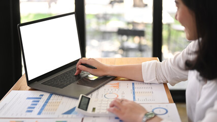 Side view of young woman economist using calculator and using laptop on wooden office desk