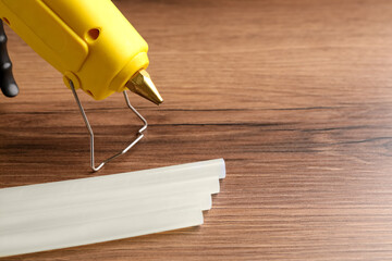 Yellow glue gun and sticks on wooden table, closeup. Space for text