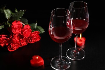 Glasses of wine, roses and heart shaped candles for romantic dinner on black table