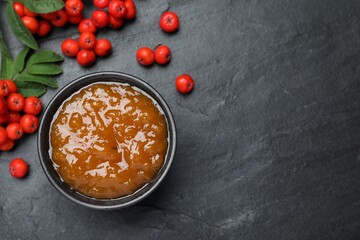 Delicious rowan jam in bowl and berries on dark table, flat lay. Space for text