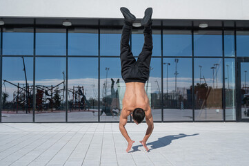 A man doing a handstand outdoors against of panoramic windows. 