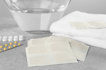 Mustard plasters, pills, towel and bowl with water on light grey marble table, closeup