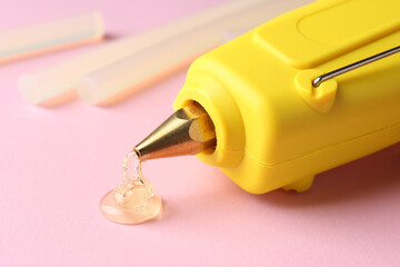 Melted glue dripping out of hot gun nozzle near sticks on pink background, closeup