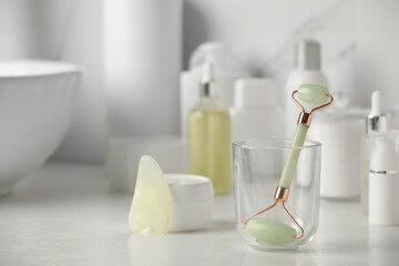 Natural face roller, gua sha tool and cosmetic products on counter in bathroom. Space for text