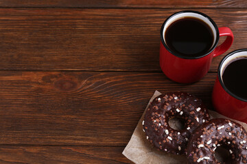 Two frosted donuts with sprinkles and cups of coffee on wooden table, space for text