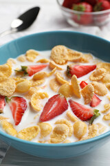 Bowl of tasty crispy corn flakes with milk and strawberries on white wooden table, closeup