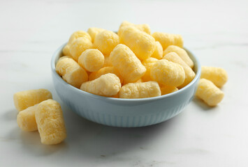 Bowl of delicious crispy corn sticks on white marble table