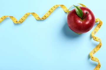 Fresh ripe red apple and measuring tape on light blue background, flat lay. Space for text