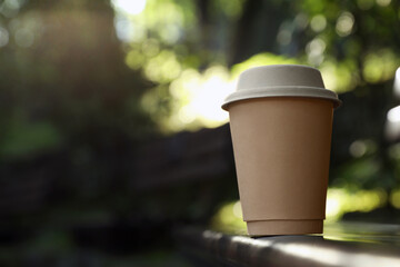 Cardboard takeaway coffee cup with lid on blurred background, space for text