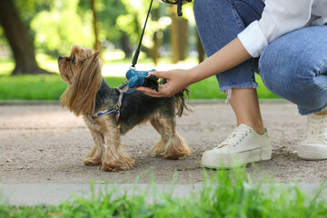 Woman with cute dog taking waste bag from holder in park, closeup