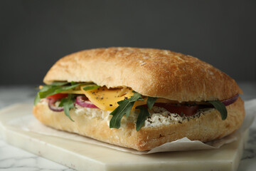 Delicious sandwich with fresh vegetables and cheese on white marble table