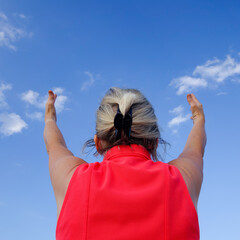 Femme blonde de dos assise sur un ballot de paille et qui tend les mains vers le ciel