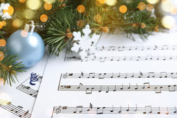 Fir branches, decorative snowflake and light blue balls on Christmas music sheets, closeup