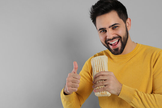 Happy young man with tasty shawarma showing thumb up on grey background. Space for text