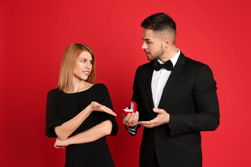 Young woman rejecting engagement ring from boyfriend on red background