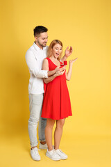 Man with engagement ring making marriage proposal to girlfriend on yellow background