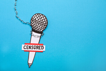 Card with word Censored, paper microphone and chain on light blue background, top view. Space for...