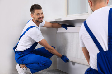 Obraz premium Professional plumbers installing new heating radiator in room