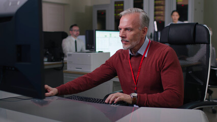 Mature engineer sit down at desk and type on computer in modern office