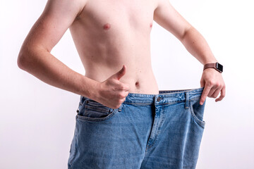 A man shows how he lost weight, big jeans on a light background, the concept of losing weight