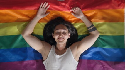 Top view of asian young man lying on rainbow flag and looking at camera