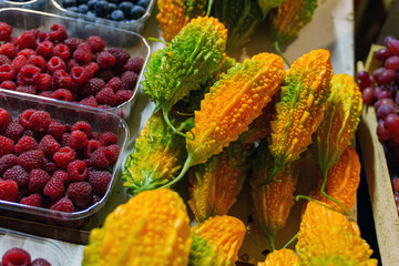 Momordica fruit of yellow-green color lies on the counter next to raspberries and cherries
