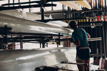 Sportsman single scull man rower sportsman checking carbon surface of boat.