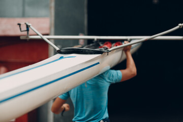 Sportsman single scull man rower prepare to competition carry boat on shoulder with muscular hand © primipil