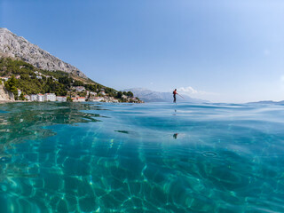 Man on the paddle board moving across beautiful, crystal clear Adriatic sea at the Mimice beach,...