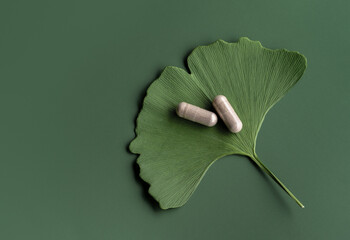 Ginkgo leaf with pills for brain, memory protect therapy and treatment of dementia. Ginkgo Biloba composition on green background, natural ingredient for alternative medicine, top view. - 526283328