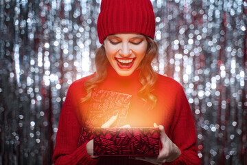 Portrait of surprised woman in red hat holding shiny christmas present gift box