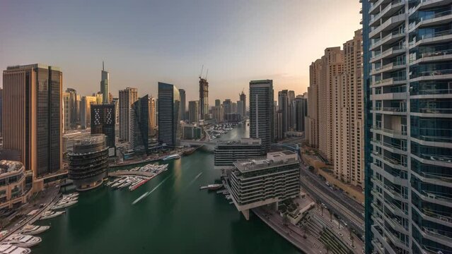 Aerial view to Dubai marina skyscrapers around canal with floating boats during all day timelapse. White boats are parked in yacht club. Shadows moving fast