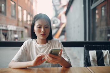 Fototapeta premium Portrait of asian woman enjoying using mobile phone sitting at outdoor cafe.