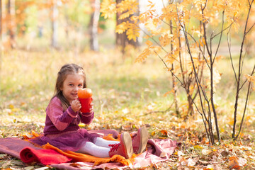 Cute little girl in autumn park with orange color leaves and yellow pumpkin