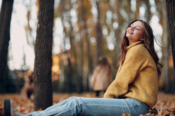 Young woman model sitting in autumn park with yellow foliage maple leaves. Fall season fashion