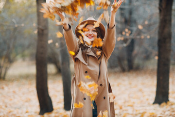 Young woman model in autumn park throw up yellow foliage maple leaves. Fall season fashion
