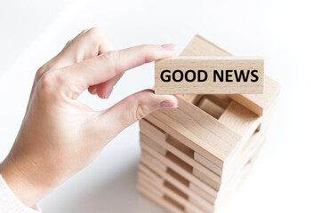 Good news text on a wooden bar in a man's hand on a light background with a tower of jenga cubes