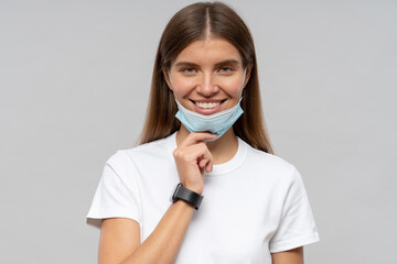 Portrait of woman pulling medical mask down in the end of covid-19 pandemic on gray background