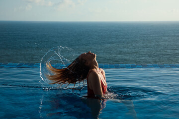 Naklejka premium Young woman in red swimsuit tossing hair out of the water