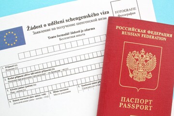 Schengen visa application form in Russian and Czech language and passport on blue background. Prohibition and suspension of visas for tourists to travel to European Union and the Baltic States concept