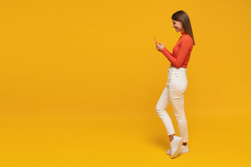 Side view of woman standing on yellow copy space background chatting online using phone - obrazy, fototapety, plakaty
